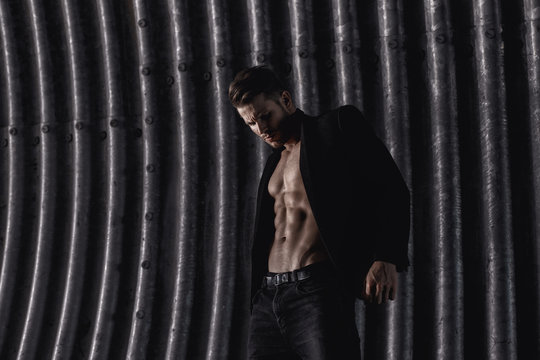 Muscular young man with beard on dark tunnel urban background. Fashion portrait of brutal strong muscle guy with modern trendy hairstyle. Model, fashion concept. Sexy naked torso, six pack abs.