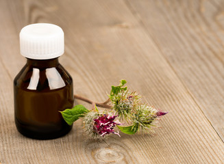 burdock flowers and essential oil in brown glass bottles on wooden rustic table