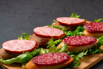 Several sandwiches with sausage and salami and sauce on a black board, background with copyspace