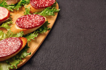 Several sandwiches with sausage and salami and sauce on a black board, background with copyspace