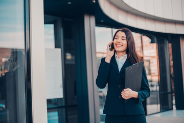 Successful smiling businesswoman or entrepreneur talking to the phone standing in front of his office.