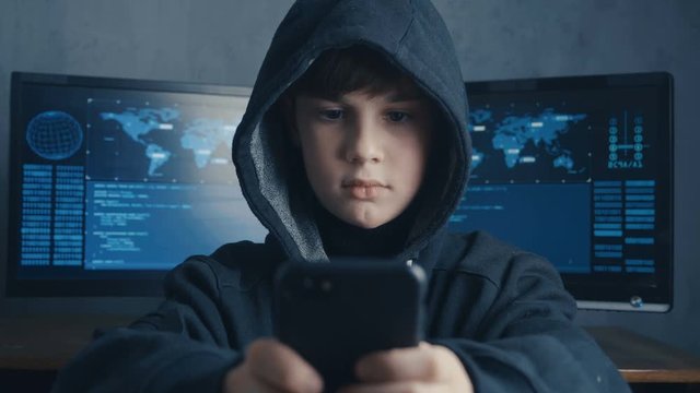 Young hooded hacker kid using a smartphone device to hijack. Genius boy wonder hacks system at cyberspace.