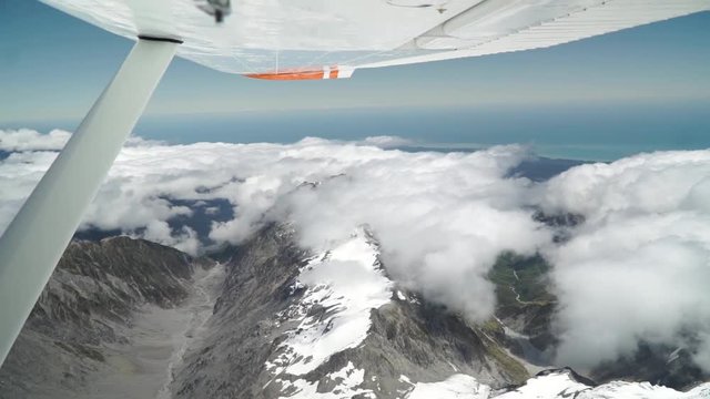 Aerial shot from plane scenic flight over west coast Franz Josef, Aoraki Mount Cook, National Park with clouds, snowcapped rocky mountains and ocean in background