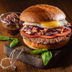 Homemade beef burger with crispy bacon and vegetables on rustic serving board