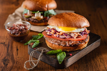 Homemade beef burger with crispy bacon and vegetables on rustic serving board