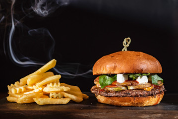 Homemade beef burger with crispy bacon and vegetables on rustic serving board