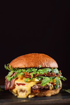 Fototapeta Homemade beef burger with crispy bacon and vegetables on rustic serving board