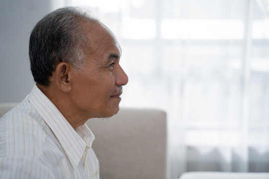 Closeup From Side View Of Asian Old Man Sitting On The Sofa A Background Of Window With Curtain