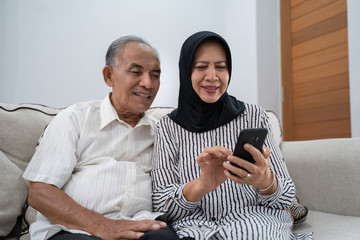 mature asian couple using modern smartphone technology at home together