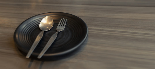 Spoon and fork in black plate placed on wooden table.