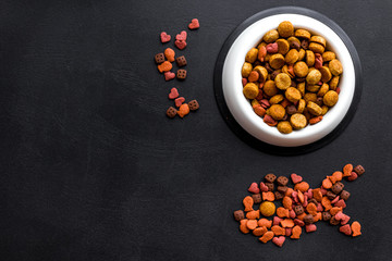 Cat food. Dry food in shape of fish, bowl with food on black backgorund top view space for text