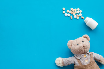 Childhood diseases concept. Treatment of children.Teddy bear toy and pills on blue background top view copy space