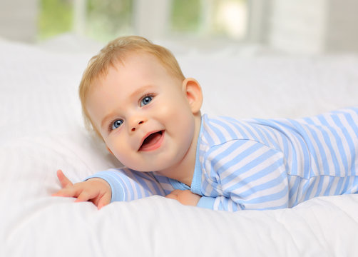 Charming blue-eyed baby 7 month old lying in bed in a striped bodysuit