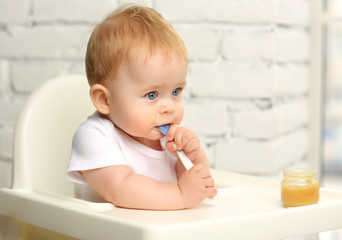 Baby 7 months in a child seat in front of the window eats food from a spoon