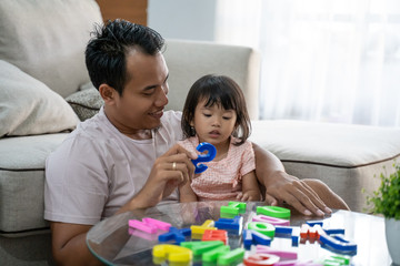 Obraz premium portrait of a patient father teaches the alphabet to his daughter by playing colorful text toys when sitting on the floor in the living room