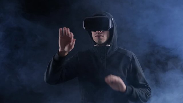 Man in hood using virtual reality headset on black smoky backgound.