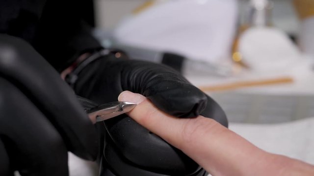 Close up macro finger nail care by manicure specialist in beauty salon. Manicurist clear cuticle professional scissors for manicure and pedicure.