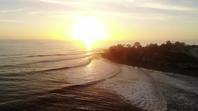 Aerial drone shot over Rincon Point surf break with ocean waves and surfers riding during sunset on the beautiful California coastline.