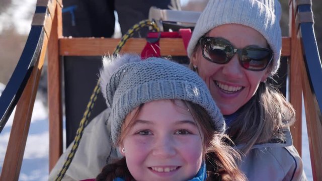 A cute young girl and her mother smiling and dogsledding through the snow on a wilderness trail in slow motion.