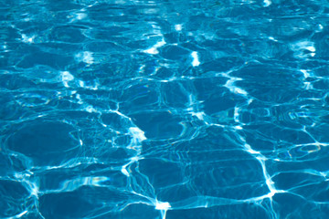 Blue and bright ripple water surface in swimming pool with sun reflection.