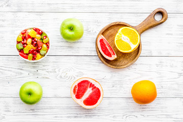 Food rich by vitamins and fiber. Healthy food. Fruit salad near fresh fruits on white wooden background top view