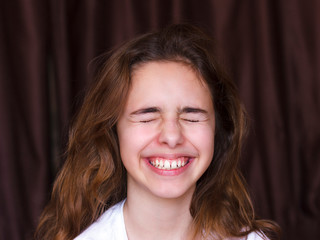 Pretty teenager girl with long hair makes very funny face and laughing with closed eyes