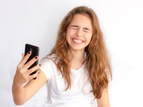 Pretty teenager girl with long hair makes selfie with funny laughing face