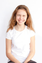 Pretty teenager girl with long hair makes very funny face and laughing with closed eyes