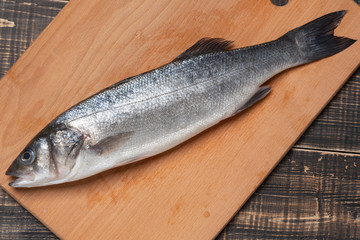 one sea fish on a wooden cutting board, fresh sea bass fish