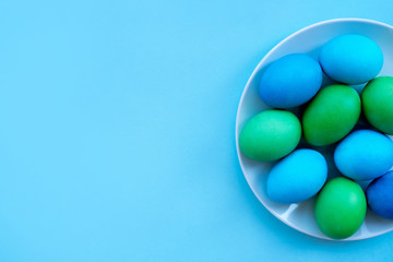 Dyied on green and blue Easter eggs on the white plate flatlay on bright blue background. Hand drawn eggs shot as a flatlay.