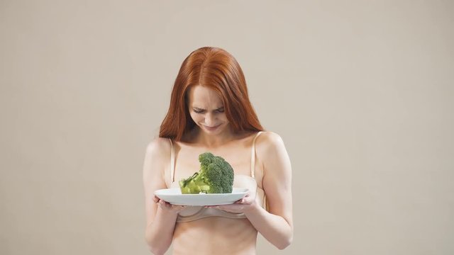 Young red-haired girl with a upset face keeps broccoli in plate, obsessed with malnutrition, afraid of excess weight, anorexia