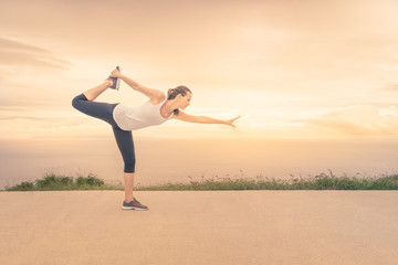 Yoga woman in serene sunset at beach doing king dancer pose. Meditation and balance exercise at sunrise or sunset.