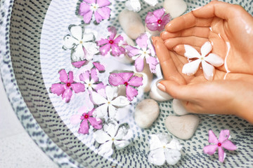 Fototapeta na wymiar Hands of Young girl with natural manicure on fingernails and bowl with water and flower.Spa treatment and massage for female hands.Close up.Spa skin and body nails care concept. Cosmetology