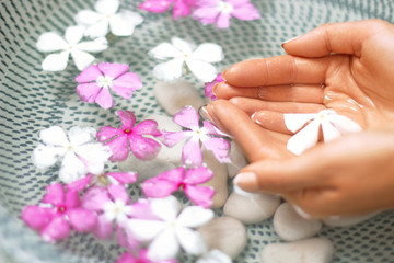 Obraz na płótnie Canvas Hands of Young girl with natural manicure on fingernails and bowl with water and flower.Spa treatment and massage for female hands.Close up.Spa skin and body nails care concept. Cosmetology.