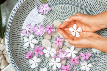 Hands of Young girl with natural manicure on fingernails and bowl with water and flower.Spa treatment and massage for female hands.Close up.Spa skin and body nails care