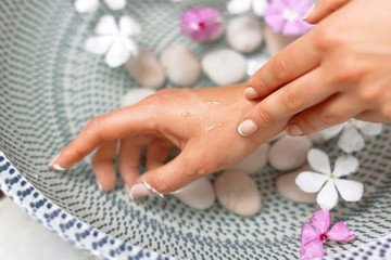 Obraz na płótnie Canvas Hands of Young girl with natural manicure on fingernails and bowl with water and flower.Spa treatment and massage for female hands.Close up.Spa skin and body nails care concept. Cosmetology.