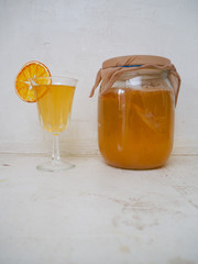 Jar and glass with fresh homemade citrus flavored kombucha tea on a counter top in a white kitchen