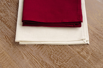 close up of cloth napkins of beige, and burgundy colors on rustic brown wooden table.