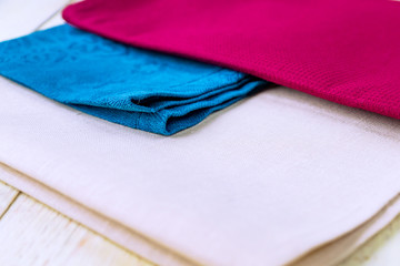 close up of cloth napkins of beige, blue and burgundy colors on rustic white wooden table. Shallow depth of field.