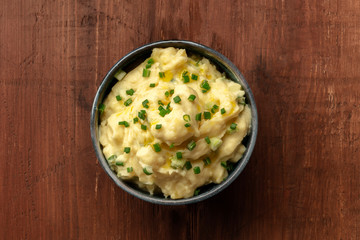 Pomme puree, a photo of a bowl of mashed potatoes with herbs, shot from above on a dark rustic background with copy space
