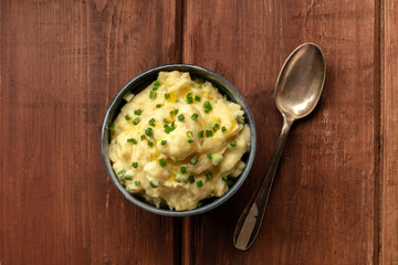 Pomme puree, a photo of a bowl of mashed potatoes with herbs, shot from the top on a dark rustic background with a spoon and copy space
