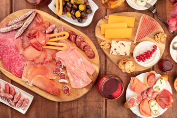Charcuterie Tasting. A photo of many different sausages and hams, deli meats, and a cheese platter, shot from the top on a rustic background with wine, olives and copy space