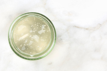 An overhead photo of a glass jar with aloe vera gel on a white marble background with a place for text
