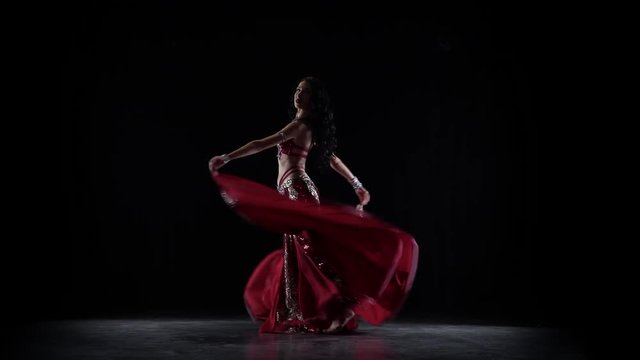 Traditional oriental belly dancer girl dancing in chiffon red dress . Black background