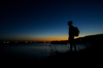 a man standing on the black sea and looking into the distance at the sunset