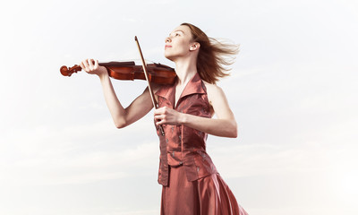 Woman violinist in red dress playing melody against cloudy sky © adam121