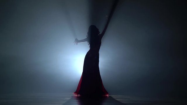 Dances belly dancing her movements. Smoke background. Sihouette