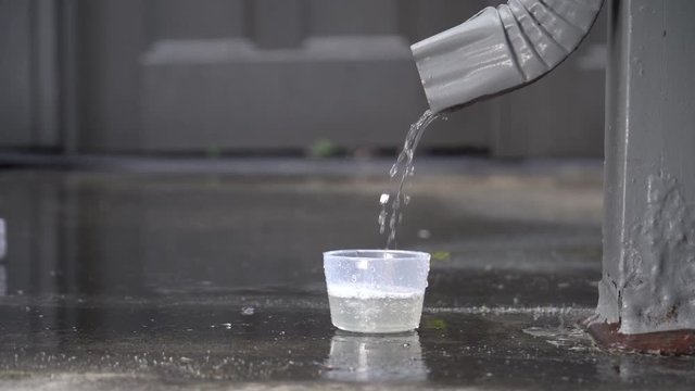 Rain water from a downspout collecting into a cup slow motion at 24fps