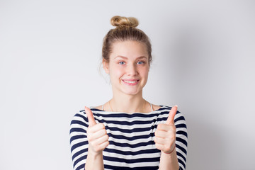 Happy and successful young business woman shows thumbs up with two hands and smiles on white background