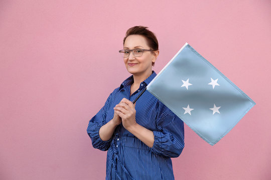 Micronesia flag. Woman holding Micronesia flag. Nice portrait of middle aged lady 40 50 years old holding a large flag over pink wall background on the street outdoors.